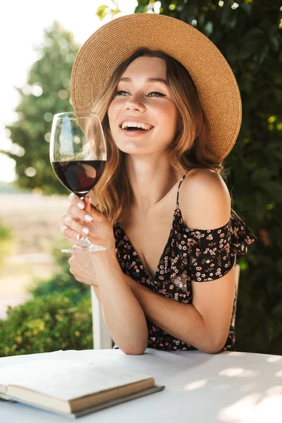 ワインを飲むガラスを保持している本と公園内のカフェの Outdors に座ってかわいいかなり若い女性の画像 — ストック写真