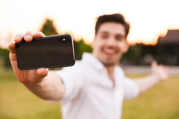 屋外若い幸せな男の画像は携帯電話で Selfie を取る 携帯電話に焦点を当てる — ストック写真