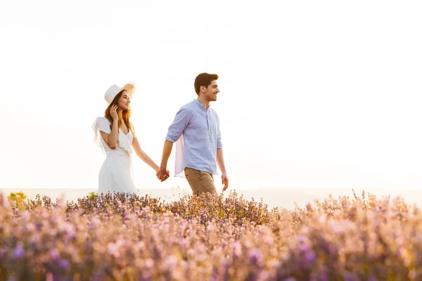 快乐的年轻可爱的情侣的形象在薰衣草领域散步在户外牵手彼此 — 图库照片
