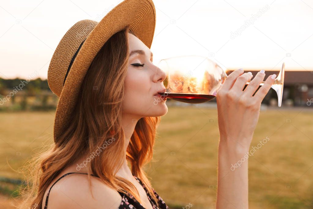 Image of cute pretty young woman outdoors holding glass drinking wine.