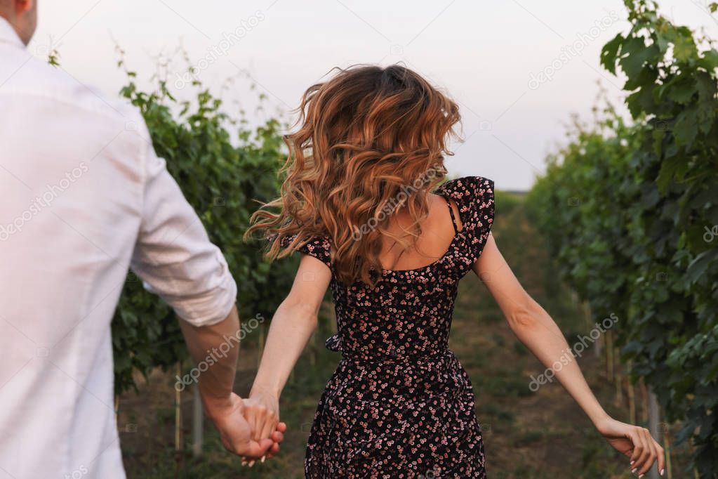 Beautiful young couple man and woman dating while walking outdoor together through vineyard on summer day