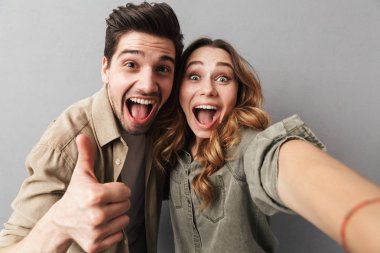 Mutlu bir genç çift ise bir selfie alarak ve başparmak gri arka plan üzerinde izole gösterilmesini sarılma portresi