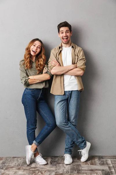 孤立した腕と共に幸せな若いカップルの立っているの完全な長さの肖像画を折り重ねグレー — ストック写真
