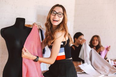 Manken ile çalışan mutlu genç kadın giysileri tasarımcı arka plan üzerine meslektaşları ile çalışan atelier stüdyosunda