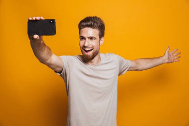 Boşaltmak gösterilen smartphone tarafından bir selfie yapmak imge-in yakışıklı neşeli adam sarı duvar backgroung üzerinde izole ayakta.