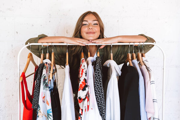 Красивая молодая женщина дизайнер одежды стоя у стойки одежды в помещении
