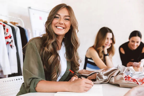 Tres Jóvenes Alegres Diseñadoras Ropa Trabajando Juntas Taller Sentadas Mesa — Foto de Stock