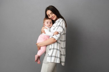 Küçük bebek kızı gri arka plan üzerinde sarılma neşeli bir genç anne portresi