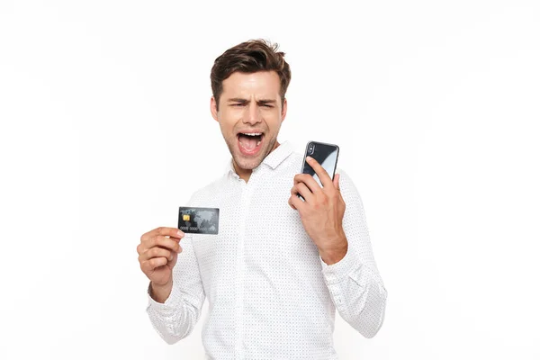 一个开朗的年轻人在衬衫持有移动电话和信用卡隔离白色后台的肖像 — 图库照片