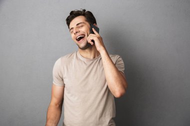 Gri artalan üzerinde izole t-shirt üzerinde cep telefonu konuşurken neşeli bir genç adam portresi