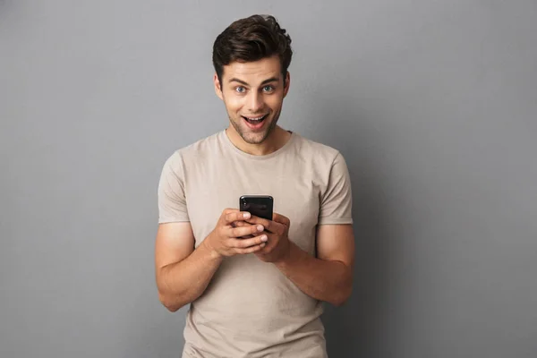 シャツ灰色の背景上分離された携帯電話を使用しての幸せな若い男の肖像 — ストック写真