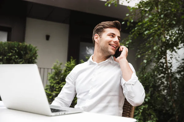 Uśmiechnięty Młody Biznesmen Ubrany Koszulę Rozmowy Telefon Komórkowy Siedząc Laptopa — Zdjęcie stockowe
