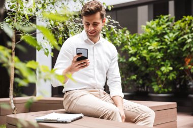 İstimal hareket eden telefon, açık havada oturma giyinmiş gülümseyen genç erkek Yöneticisi resmi