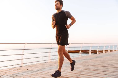 Şort ve tişört iskele veya boardwalk, sahil boyunca gündoğumu sırasında çalışan kas sportif adam 20'li yaşlarda görüntüsünü