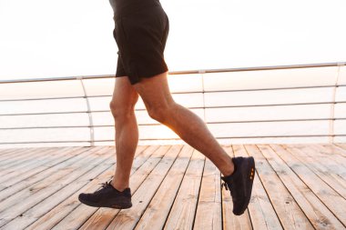 Kas sportif adamın 20'li yaşlarda şort ve tişört iskele veya boardwalk, sahil boyunca sabah çalışan fotoğraf kırpılmış