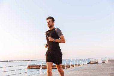 Şort ve tişört iskele veya boardwalk, sahil boyunca gündoğumu sırasında çalışan mutlu sporcu 20'li yaşlarda görüntüsünü