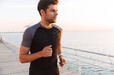 Görüntü gündoğumu sırasında iskele veya boardwalk, sahil boyunca eşofman koşu içinde kas yakışıklı adamın 20'li