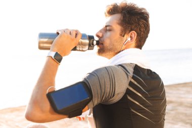Runner adamın 20'li eşofman sahil ve Termos Kupa içme suyu ahşap iskele üzerinde oturan smartphone kol sahibi ile fotoğraf