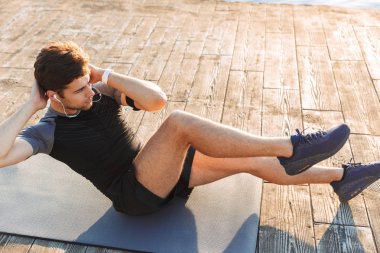Fotoğraf genç sportif adamın 20'li eşofman mindere yalan ve criss yapıyor egzersizi üzerinde çalışırken ahşap iskelesi sahil'sabah çapraz