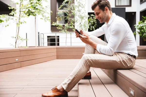 Atractivo Joven Gerente Masculino Formal Vestido Sosteniendo Teléfono Móvil Sentado — Foto de Stock