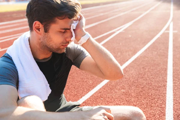 Exhausted sportsman finished running at the stadium, wiping face with towel