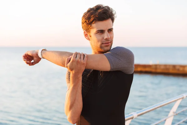 ショート パンツや シャツ ウォーミング アップや朝の海辺近くの腕をストレッチ運動スポーティな男 代のイメージ — ストック写真