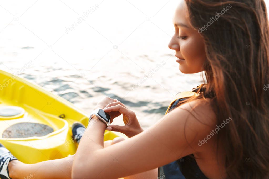 Young woman kayaking on lake sea in boat using her watch clock on hand.