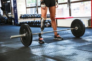 Atletik beyaz Engelli Kadın protez eğitim ve spor salonunda halter kaldırma eşofman giyiyor kırpılmış görüntü