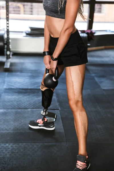 Portrait of fitness disabled woman with prosthesis in sportswear doing crossfit exercises and lifting dumbbell in gym