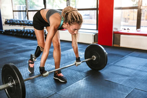 Portrait of european sporty disabled woman wearing prosthesis in tracksuit training and lifting barbell in gym