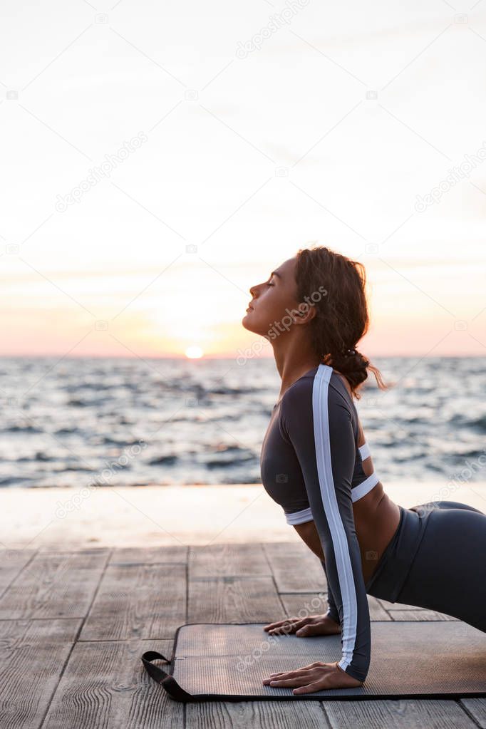 Image of amazing strong young fitness woman outdoors in the beach make yoga stretching exercises.