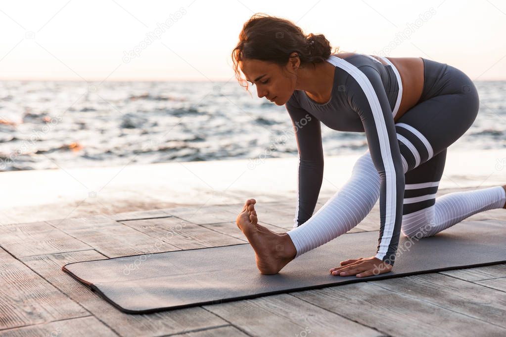 Picture of young fitness lady outdoors in the beach make yoga stretching exercises.