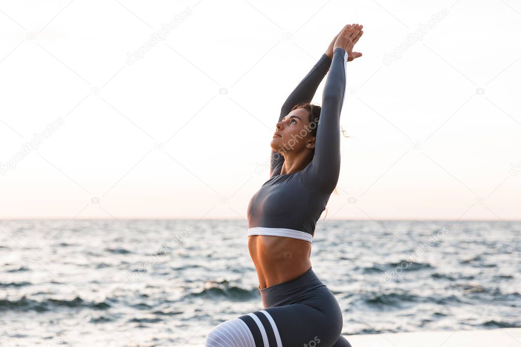 Image of amazing strong young fitness woman outdoors in the beach make yoga stretching exercises.