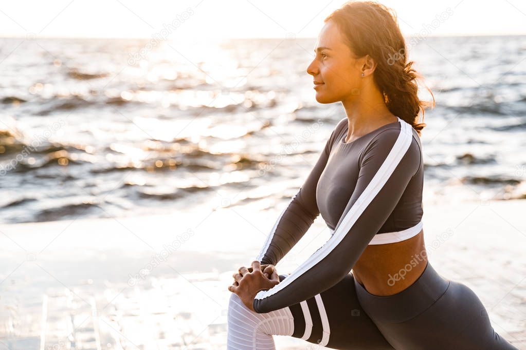 Image of concentrated young fitness woman outdoors in the beach make yoga stretching exercises.