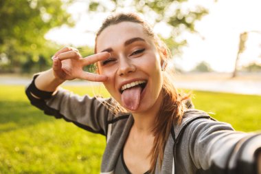 Güzel sportif 20'li kadında selfie parmak ile yeşil parkta yürürken alarak bluetooth earpod giyiyor spor fotoğrafı