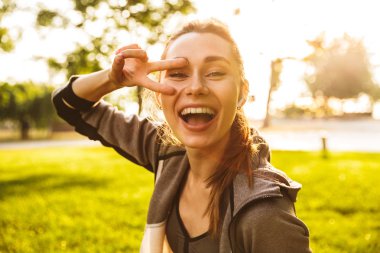 Mutlu sportif 20'li kadında selfie parmak ile yeşil parkta yürürken alarak bluetooth earpod giyiyor spor fotoğrafı