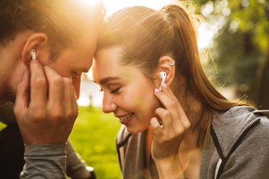 Mutlu genç insanlar erkek ve kadın 20'li eşofman yeşil parkta yürürken müzik kulaklık ile birlikte dinlemek içinde görüntü