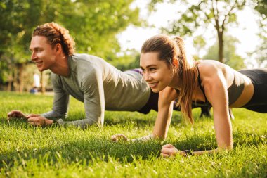 Fotoğraf güzel sportif çift erkek ve kadın 20'li yaşlarda tahta birlikte yeşil park eğitim sırasında güneşli yaz gün süre çimenlerin üzerinde yaptığı spor giyim