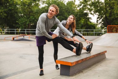 Görüntü atletik sportif çift erkek ve kadın 20'li yaşlarda çalışma dışarı ve skate park vücut germe eşofman