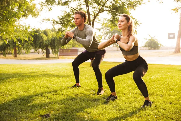 年轻的白种人运动的男人和女人的形象20S 在运动服做锻炼和蹲在绿色公园在晴朗的夏天天 — 图库照片