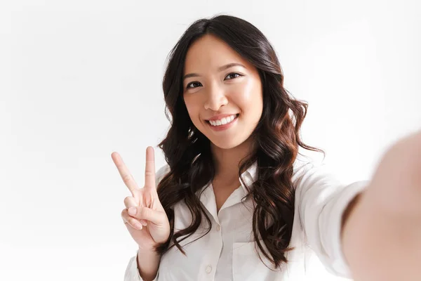 乐观的中国妇女的肖像微笑着 拿着自拍照片与和平标志隔离在白色背景在演播室 — 图库照片