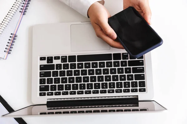 空白の画面携帯電話を保持しているラップトップ コンピューターを机の上に座っている白いシャツの女性のクローズ アップ — ストック写真