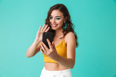 İçerik mutlu kadın 20'li yaşlarda gülümseyen ve mavi arka plan üzerinde izole selfie çekerken fotoğraf makinesi vasıl el sallayarak glamour tarzı ile fotoğrafı