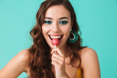 Güzel mutlu kadın 20'li yaşlarda gülümseyen ve mavi arka plan üzerinde izole lolipop yemek oynak bakışla portresi