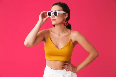 Fotoğraf güneş gözlüğü dokunmaktan ve pembe arka plan üzerinde bir kenara izole seyir glamour kafkas kadın 20'li yaşlarda giyen moda küpe
