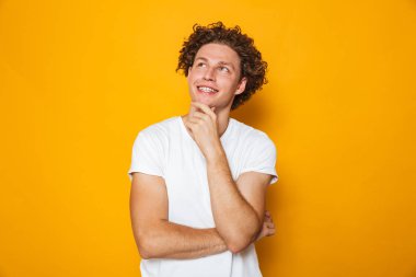 Uzak izole sarı arka plan üzerinde arıyorsunuz bir gülümseyen dalgın kıvırcık saçlı adam portresi