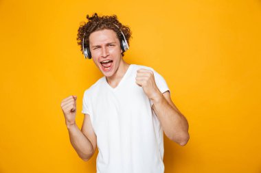 Kulaklıklar ve sarı arka plan üzerinde izole şarkı ile müzik dinlemek kıvırcık saçlı esmer neşeli adam fotoğrafı