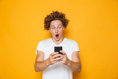 Casual beyaz t-shirt smartphone vasıl bakarken çığlık izole sarı arka plan üzerinde beyaz adam heyecanlı