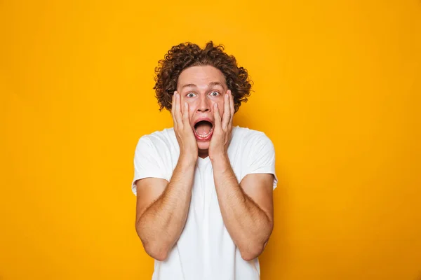 Portrait of a shocked curly haired man screaming isolated over yellow background