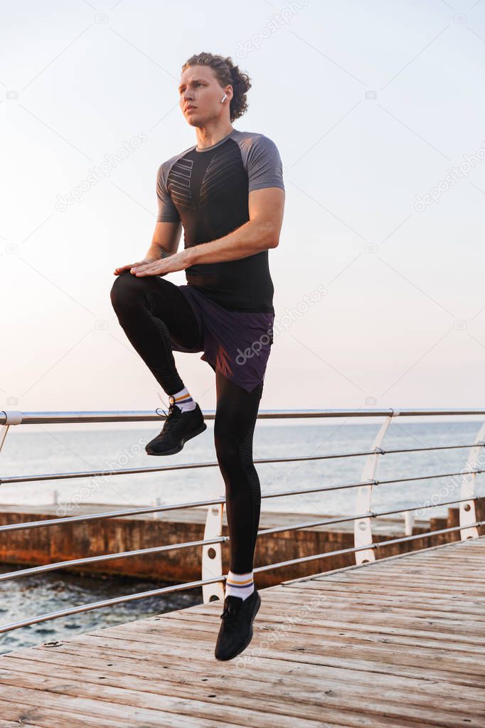 Photo of handsome strong young sportsman outdoors at the beach make exercises.